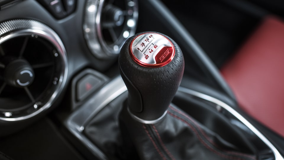 El interior de un Camaro decorado con una perilla de cambios color Rojo, costuras color Rojo y superficie de los asientos color Rojo.