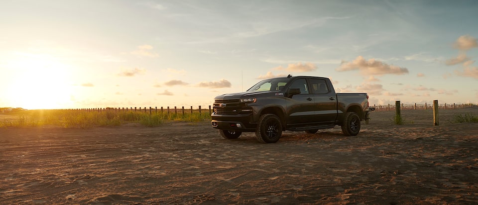 A gray Silverado LT Trail Boss sits in a parking lot backlit by the rising sun.