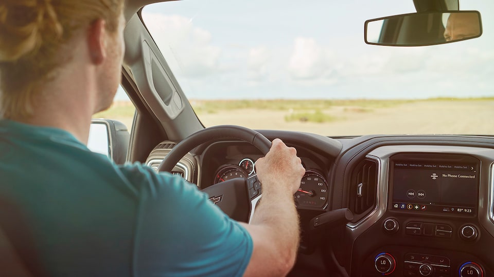 Seen from the backseat of a Chevy Silverado, a man in a green t-shirt is driving through a coastal area.