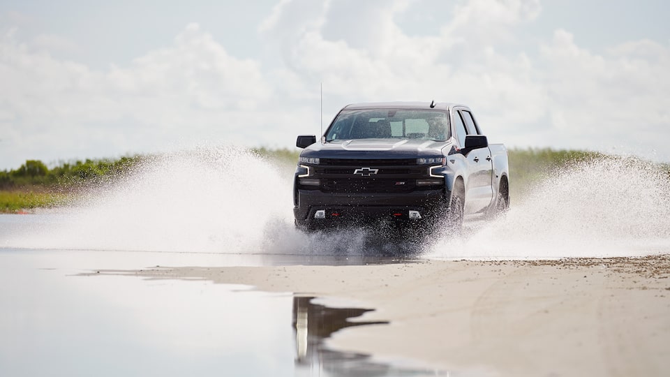 A gray Silverado LT Trail Boss raises water on both sides as it drives along the edge of a backwater area.