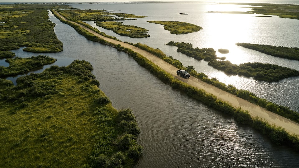An aerial view of a Silverado LT Trail Boss driving on a dirt road between two backwater areas along the coast.