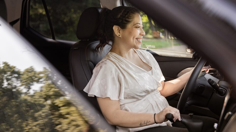 Viewed from outside a partly open front passenger window, Joanna Bonilla smiles as she drives her Traverse.