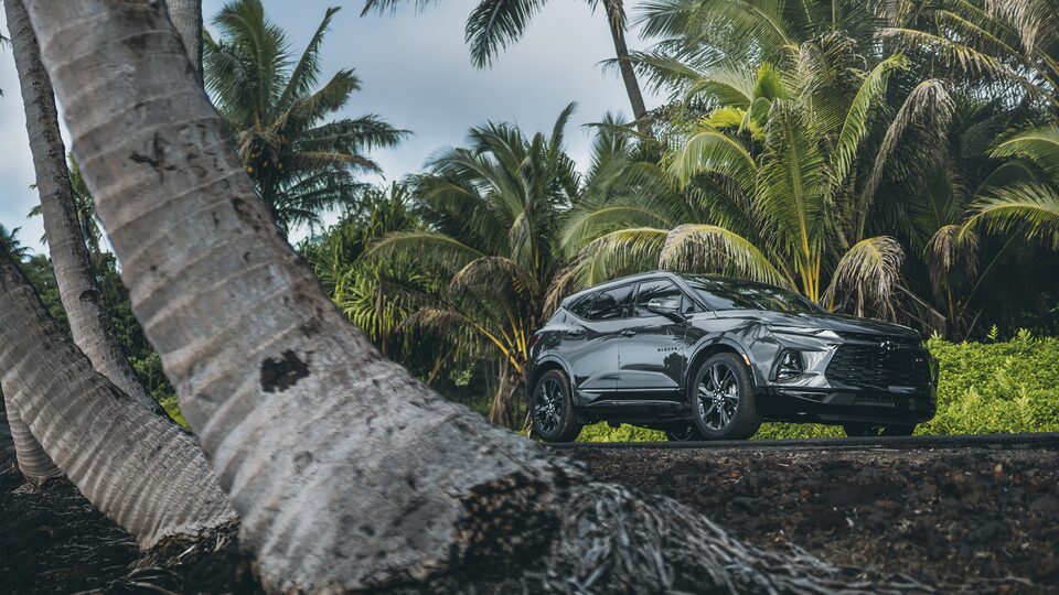 Una Chevy Blazer RS en Gris Hierro Metálico va por un camino en Hawái rodeado de vegetación y palmeras.