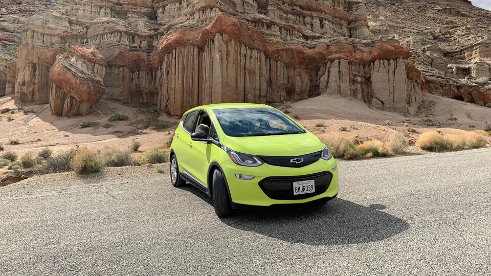 A photo of Nicole Dome’s Shock green Bolt EV on a gravel road among red rock outcroppings.