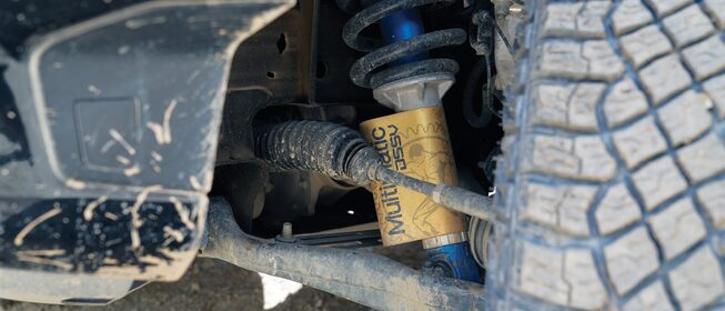 Primer plano de la parte superior de un neumático cubierto de tierra y los amortiguadores Multimatic DSSV de una Silverado ZR2.