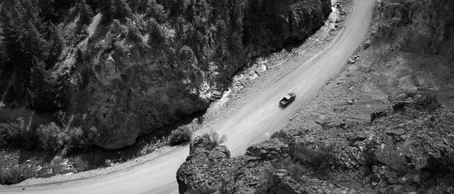 Vista desde arriba, una Silverado ZR2 anda por un camino de tierra en un cañón de montaña. Se ve la silueta de la 2 contra un sol poniente, con polvo levantándose alrededor del vehículo.