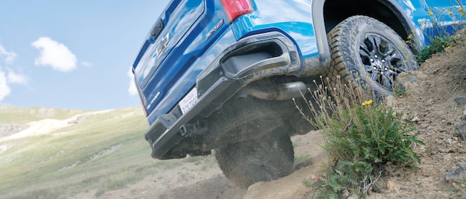 Primer plano de la parte trasera de una Silverado ZR2 azul andando a través de la maleza en una zona montañosa.