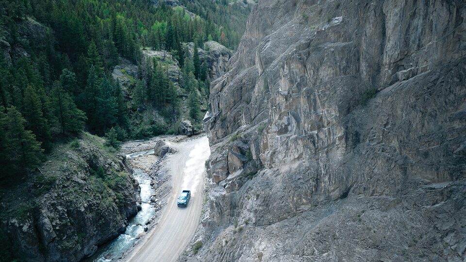 Vista arriba desde la distancia, una Silverado ZR2 levanta polvo mientras recorre un camino de tierra en un cañón de montaña.