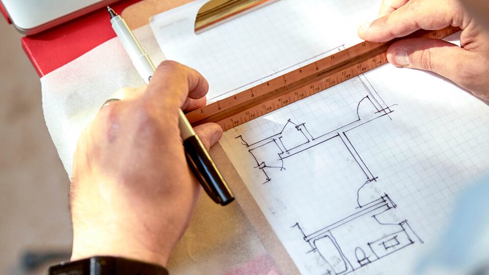 Close-up of Jon Hagar’s hands holding a pen and ruler above an architectural sketch on grid paper.