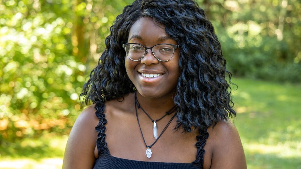Kosis Ifeji, standing in a wooded area, smiles at the camera.