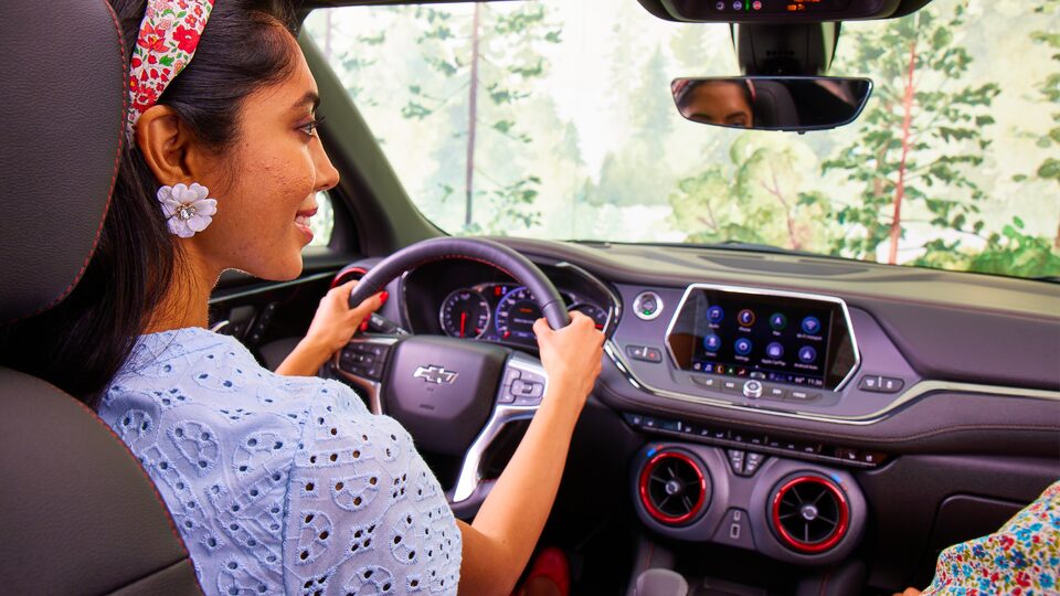Desde el asiento trasero, una mujer sonríe mientras está sentada en el asiento del conductor de una Chevy Blazer 2021.