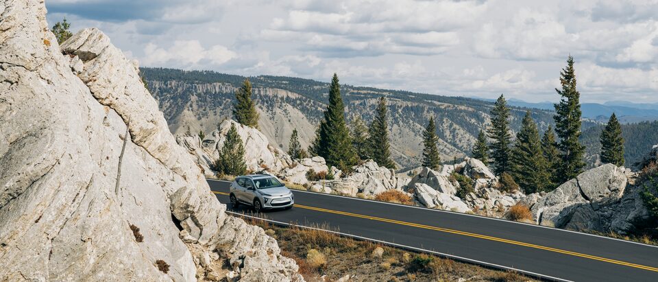 Una Bolt EUV color blanco rodea una curva en el Parque Nacional Yellowstone y emerge por detrás de una formación rocosa, con un fondo boscoso.