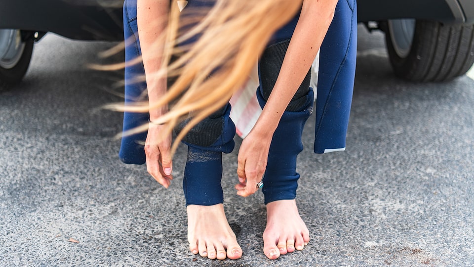 A woman with long blond hair sits in the back of a Bolt EV putting on a wetsuit.