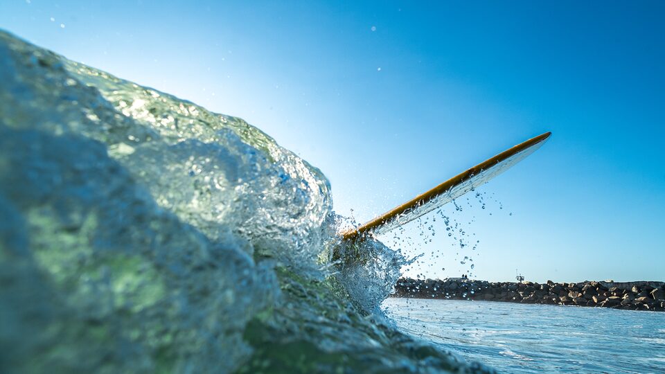 A surfboard emerges from a wave in the ocean.