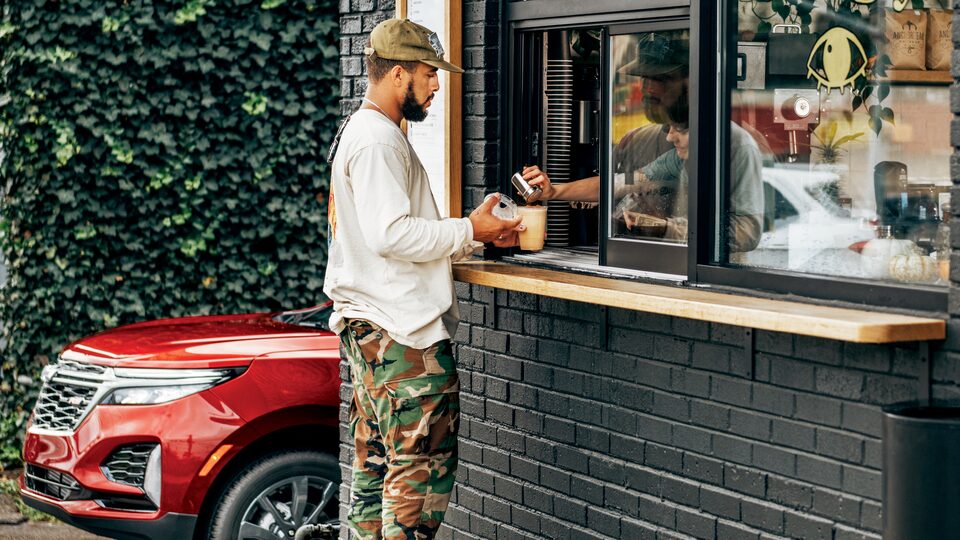 Brad Frey stands at the service  window of a coffeeshop getting  a cup of coffee.