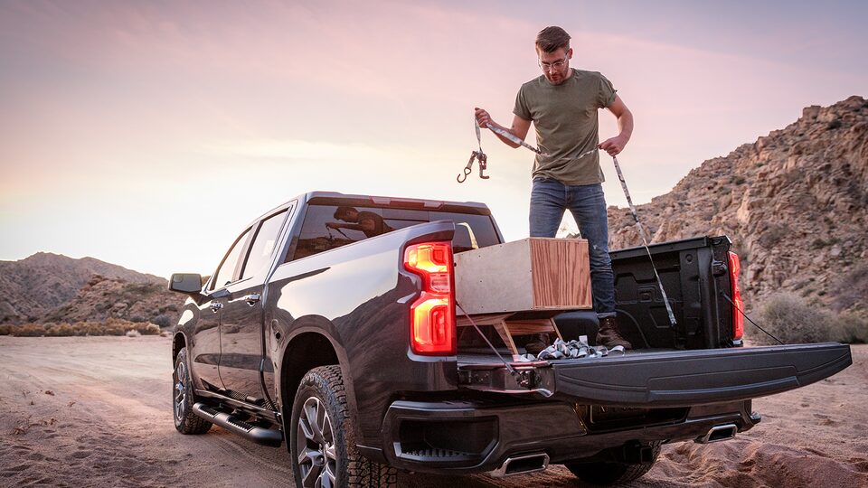 Un hombre con ropa de trabajo está parado en la caja abierta de una camioneta pickup Chevy Silverado en Negro. Está ajustando algunas maderas en la caja.