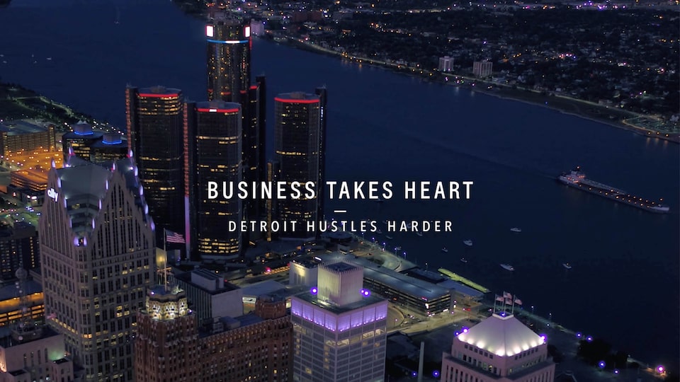 A bird’s-eye nighttime view of the Detroit skyline, with the text “Business Takes Heart - Detroit Hustles Harder” over the image.