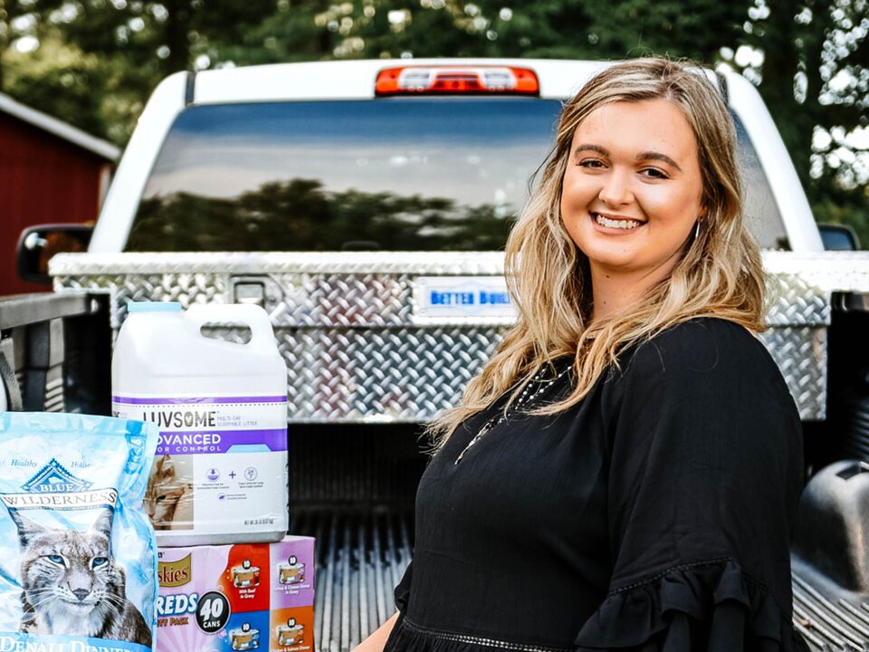 Scout Bagley stands at the open tailgate of her Silverado, which has several bags of pet food in the bed.