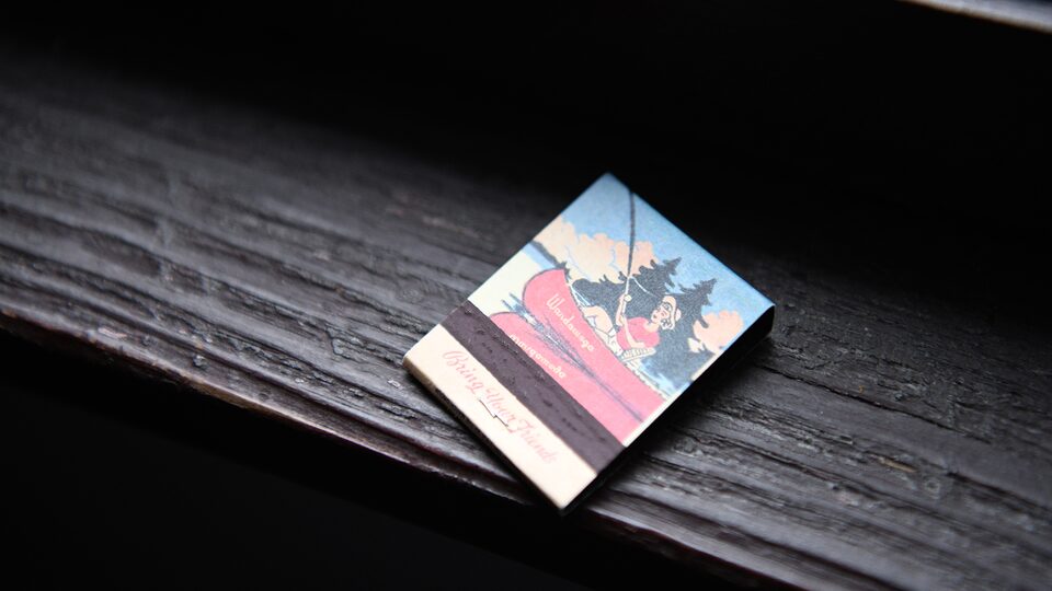 Una caja de fósforos con el dibujo de una escena serena de una canoa en un lago reposa sobre una mesa de madera.