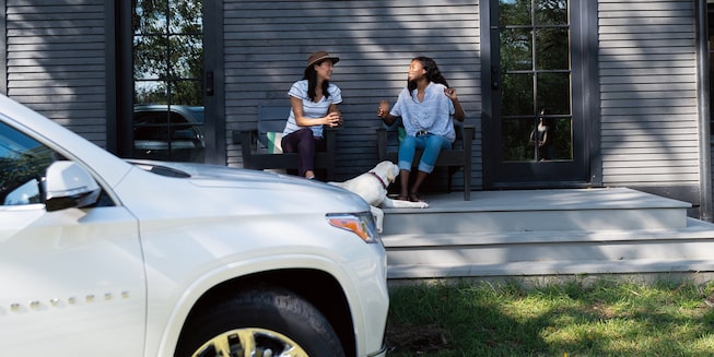 dos mujeres se sientan y conversan sobre el porche de una cabaña, con una Chevrolet Trverse color Blanco en el fondo.
