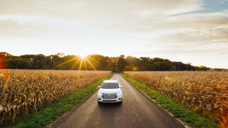 El extremo delantero de la Chevrolet Traverse mientras conduce por un camino de campo con el atardecer detrás.
