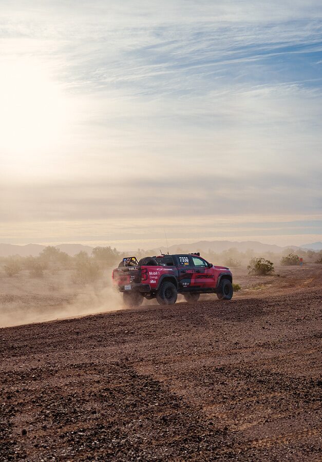 Chad Hall's Colorado ZR2 from a distance drives across a desert landscape in the dusty air.
