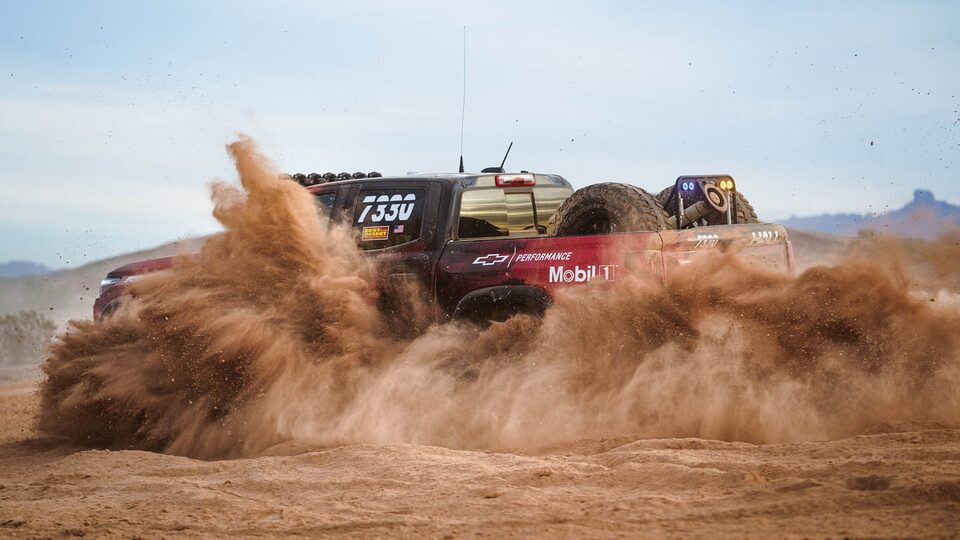 An action shot of Chad Hall driving his Colorado ZR2 in the desert, with dust and sand kicking up to halfway obscure the truck.