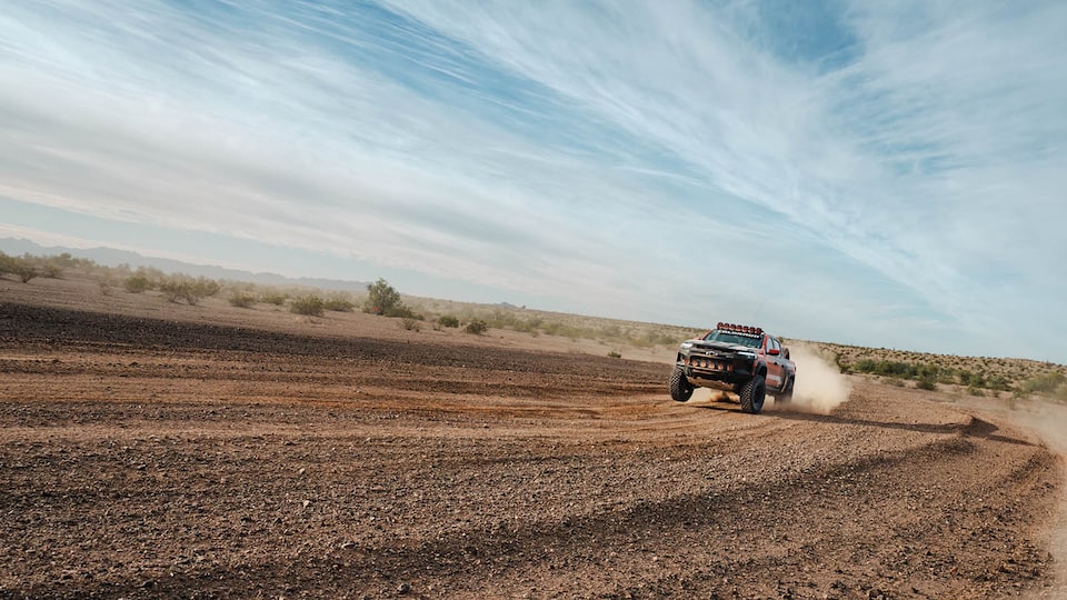 Seen at a distance, Chad Hall drives his Colorado ZR2 toward the camera in a remote desert landscape, with thin clouds striping the pale blue sky overhead.