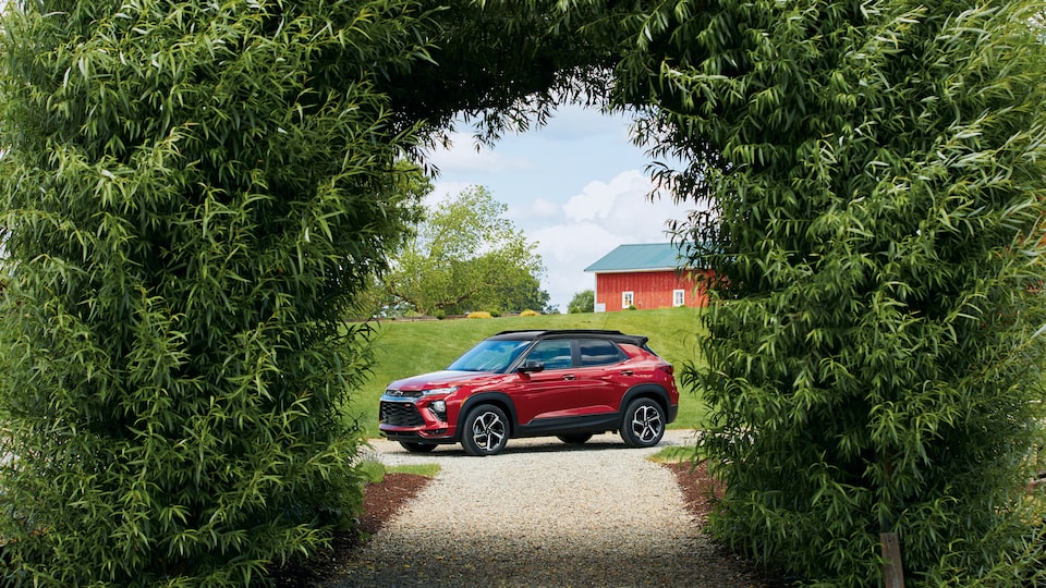 A red Chevy Trailblazer RS is framed by an arch covered with greenery, with farm buildings in the background.