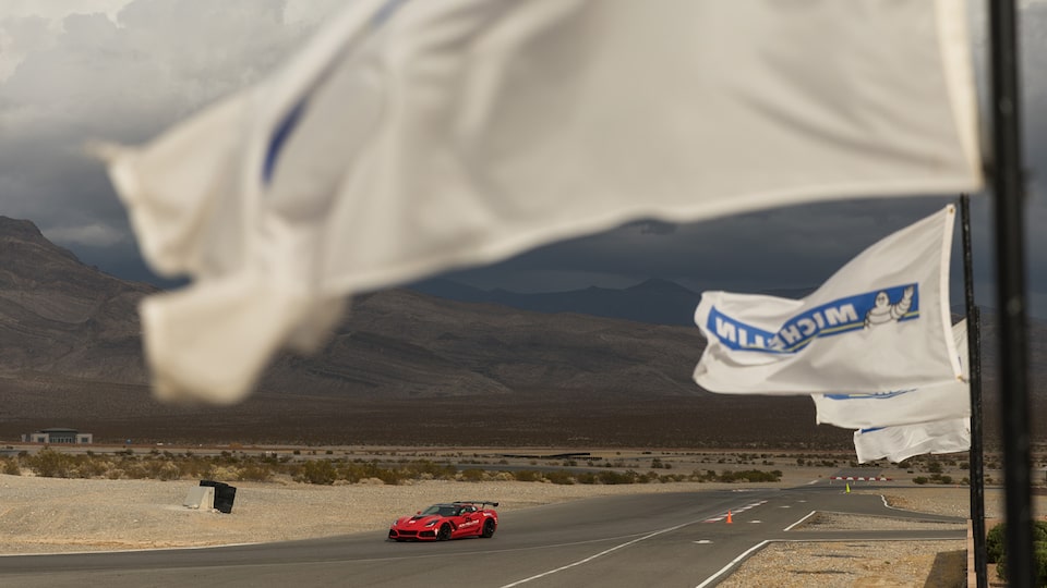 Un Corvette color Rojo en la pista con banderas Michelin blancas ondulantes en primer plano.