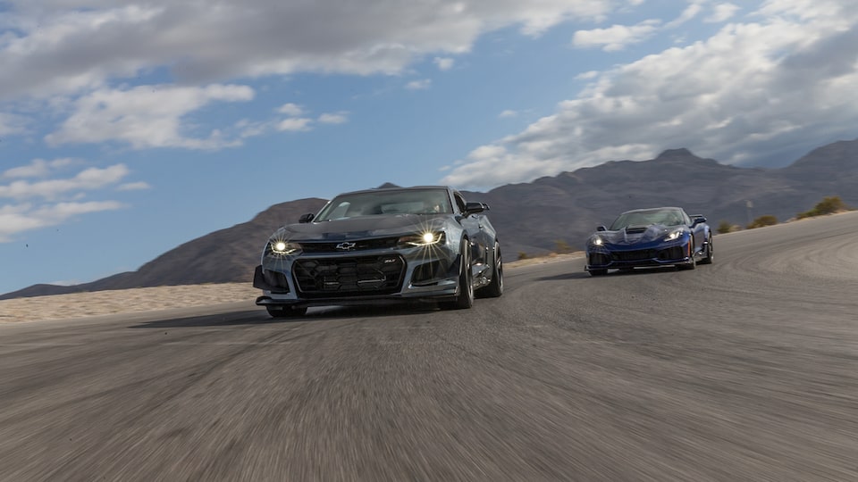 Una Camaro, con un Corvette detrás, en una pista de carreras en un centro privado en el desierto.