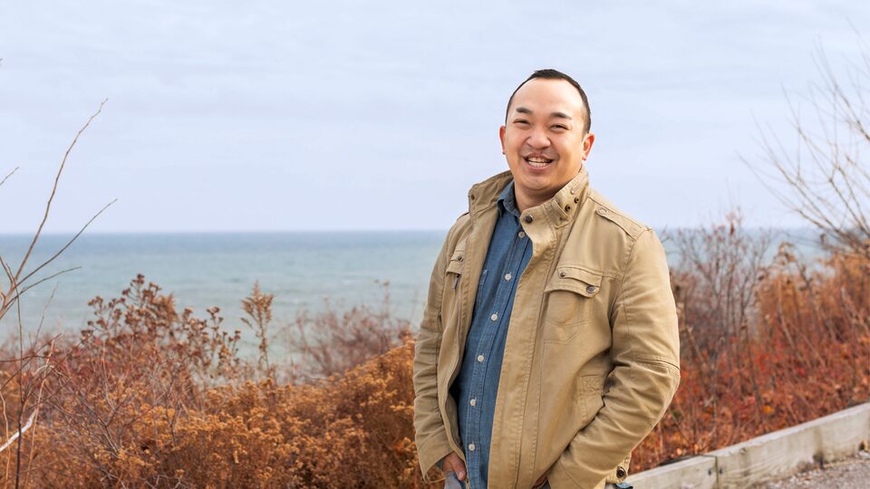 Erik Kennedy sonríe a la cámara de pie en una colina con vista al lago Michigan.