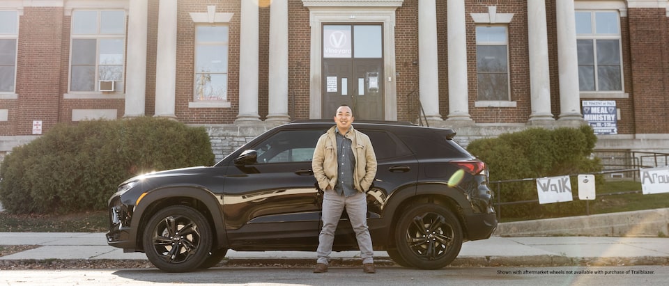 Erik Kennedy de pie frente a su Trailblazer RS 2021, que está estacionada enfrente de un edificio de ladrillos grande con columnas blancas.