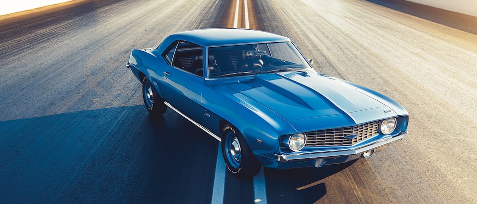 An original blue COPO Camaro sits in the middle of a road.