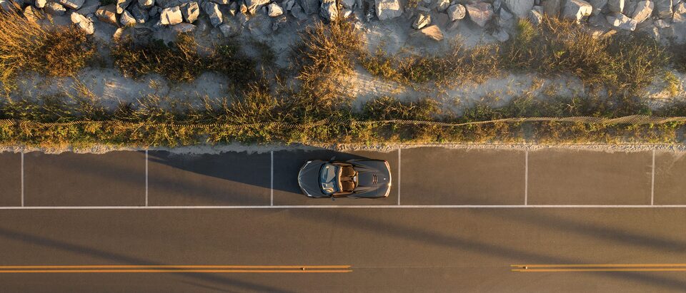 A Corvette convertible is seen from directly above on a coastal highway.