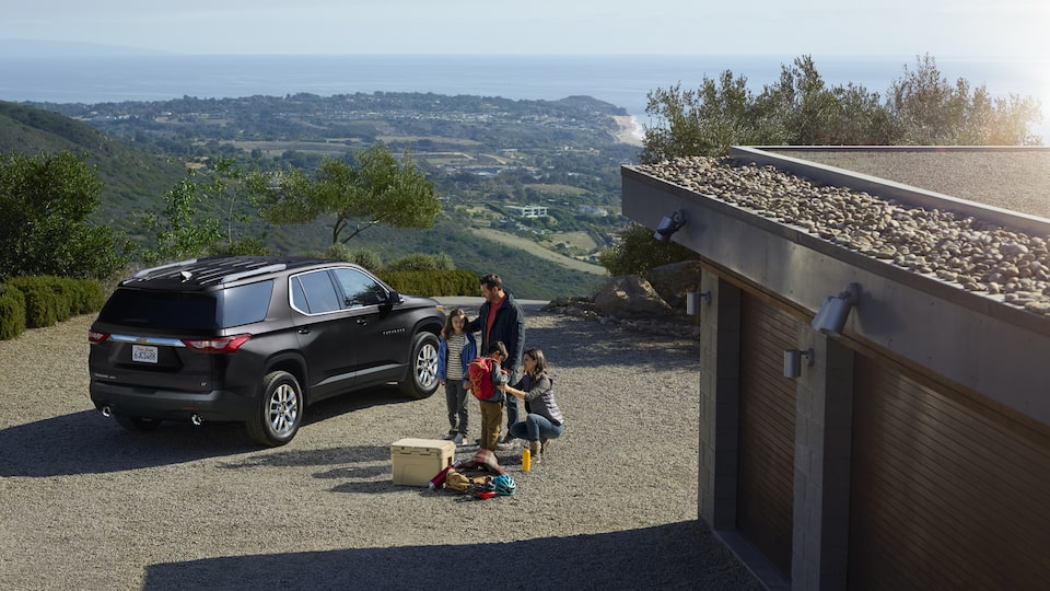 A family of four and their luggage stands outside of a Traverse.