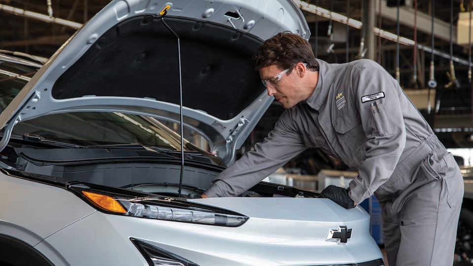 Un empleado de mantenimiento alcanza el interior del capó de un Chevy Bolt en un taller de servicio de un concesionario Chevy.