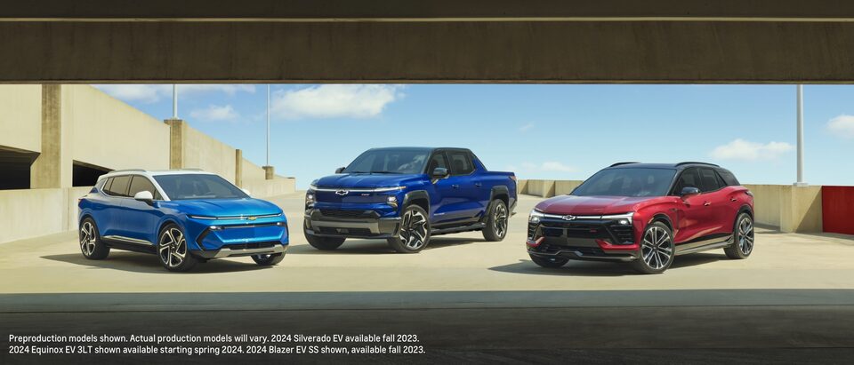 Una Equinox EV azul, una Silverado EV azul y una Blazer EV roja estacionadas juntas en el nivel superior abierto de un estacionamiento.