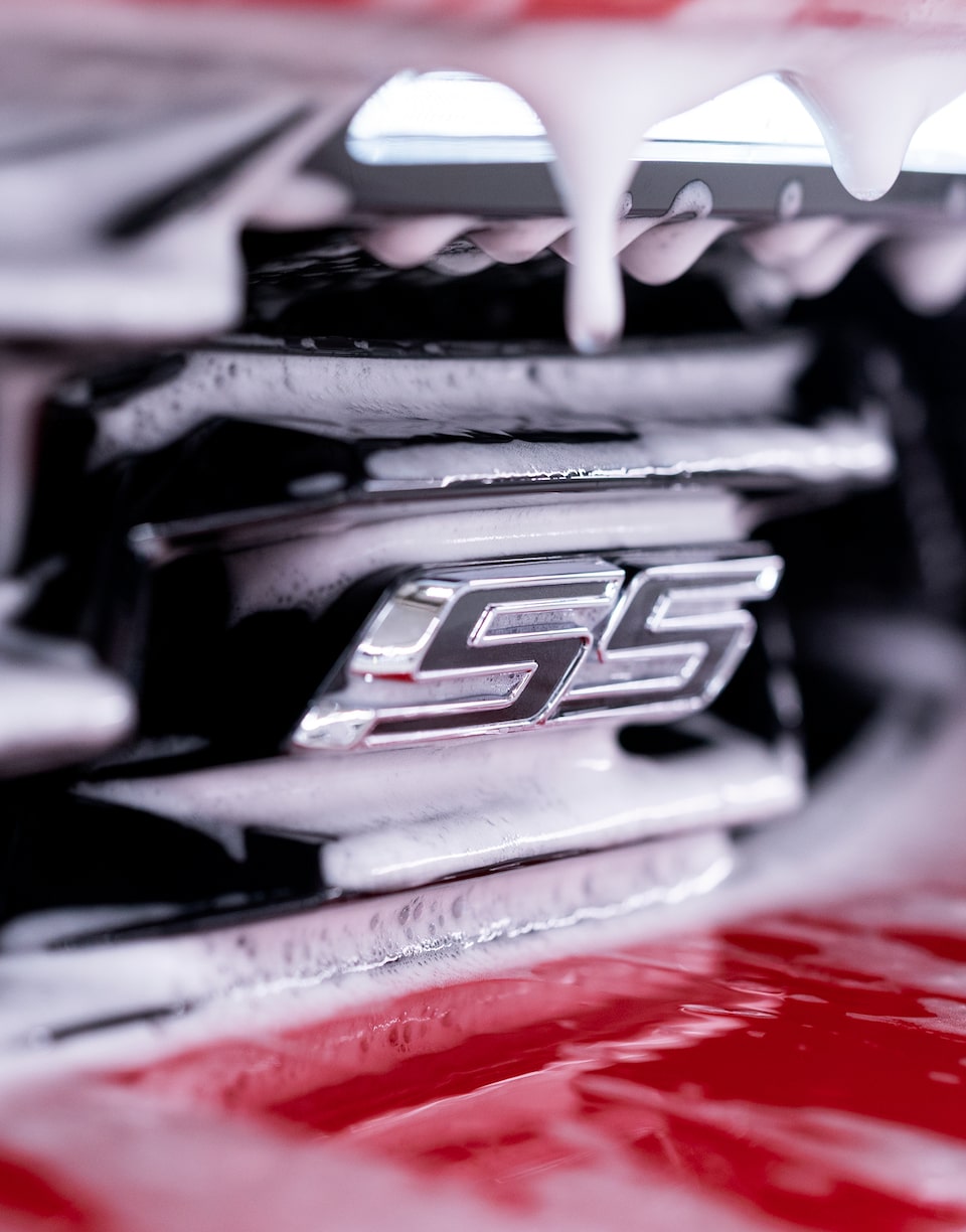 A close-up detail of the SS emblem on a Chevy Camaro with white foam in the crevices surrounding it.
