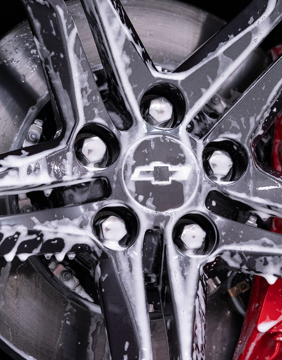 A close-up detail of a five-spoke wheel on a Chevy Camaro scattered with droplets of white foam.