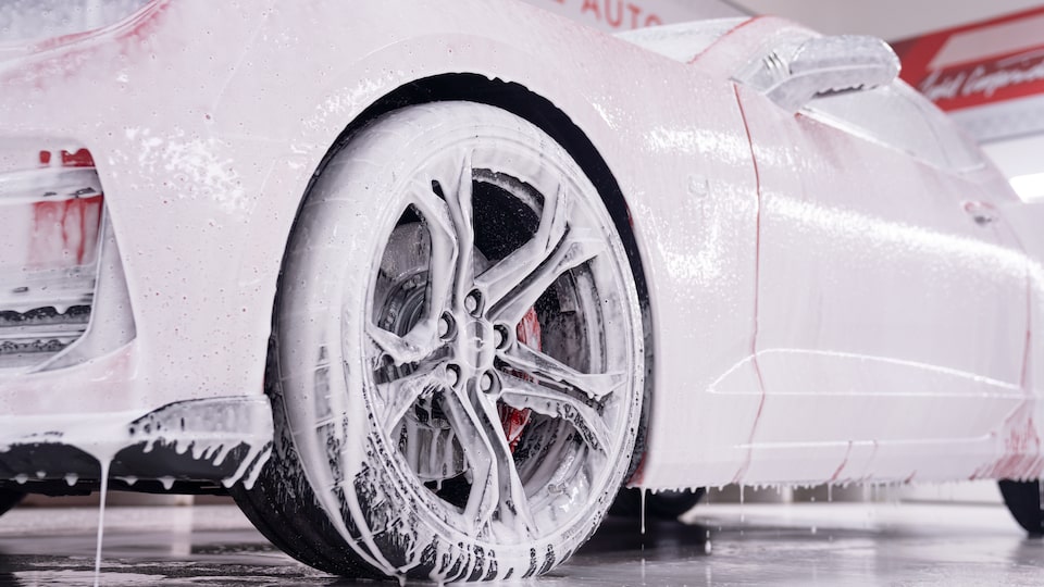 A red Chevy Camaro covered in a white foam inside the Esoteric Fine Auto Finishing shop.