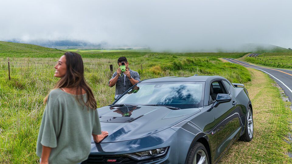 Un hombre usa una cámara Polaroid para tomar una foto de una mujer cerca del frente de un Camaro SS 2020.