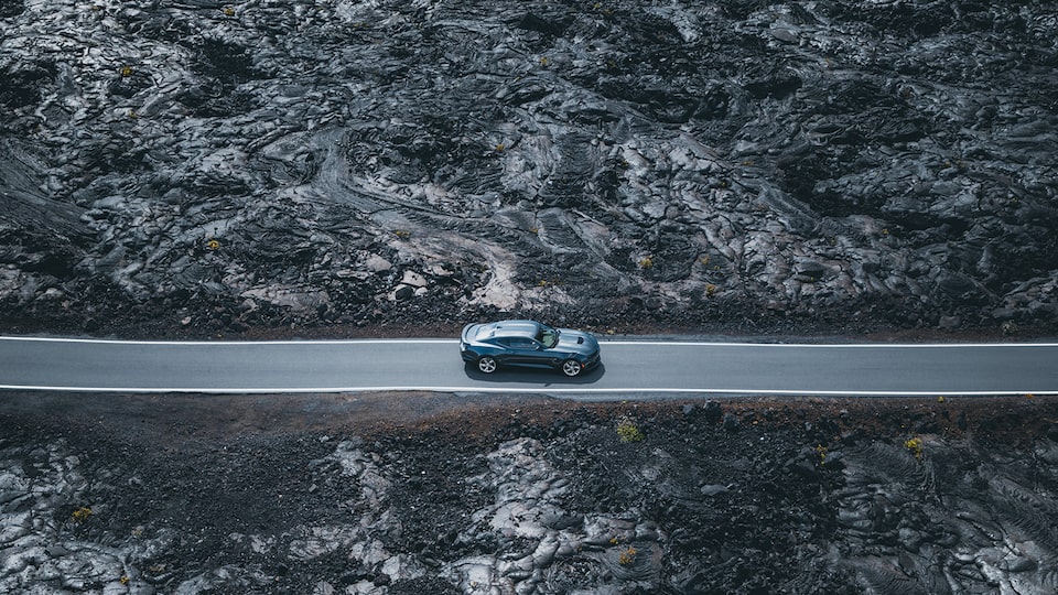 Un Camaro SS 2020 estacionado en un camino angosto, rodeado de roca volcánica negra.