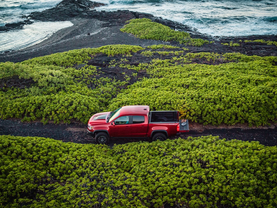 Vista lateral de una Chevrolet Colorado ZR2 roja estacionada sobre un camino angosto con vegetación de ambos lados.