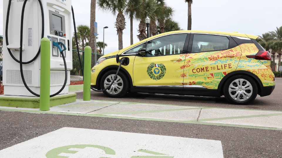 Un Chevrolet Bolt EV Cargo color Amarillo con una envoltura colorida de The Yerba Mate Company estacionado en una estación de carga.