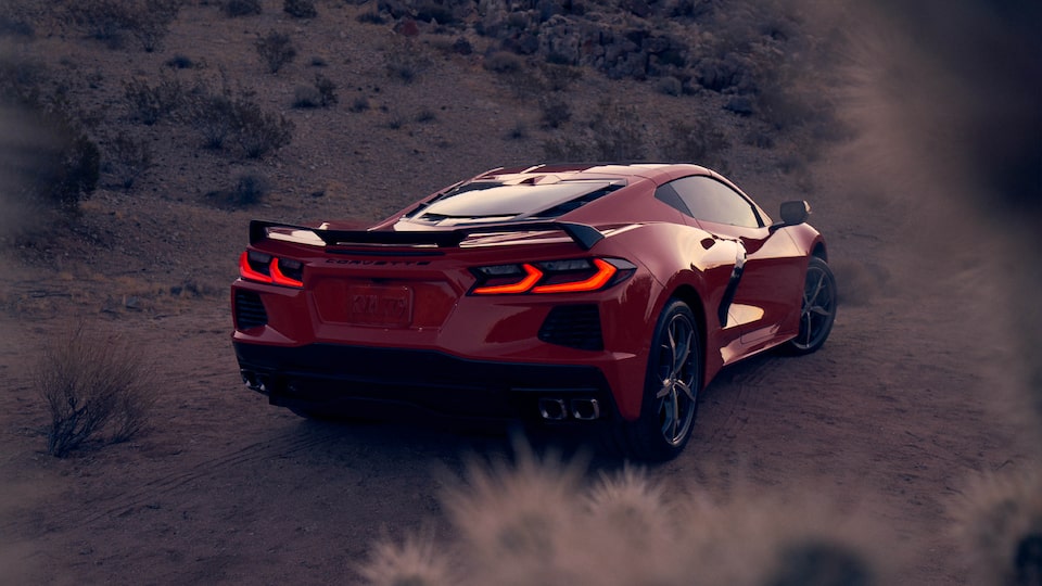 A Torch Red 2020 Corvette coupe in a desert landscape, seen from the rear with the brake lights illuminated.
