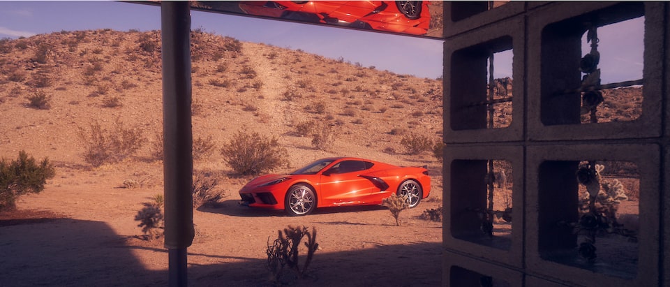 A Torch Red 2020 Corvette coupe sitting in a desert landscape, seen through a window.