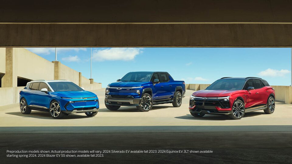 Una Equinox EV azul, una Silverado EV azul y una Blazer EV roja estacionadas juntas en el nivel superior abierto de un estacionamiento.