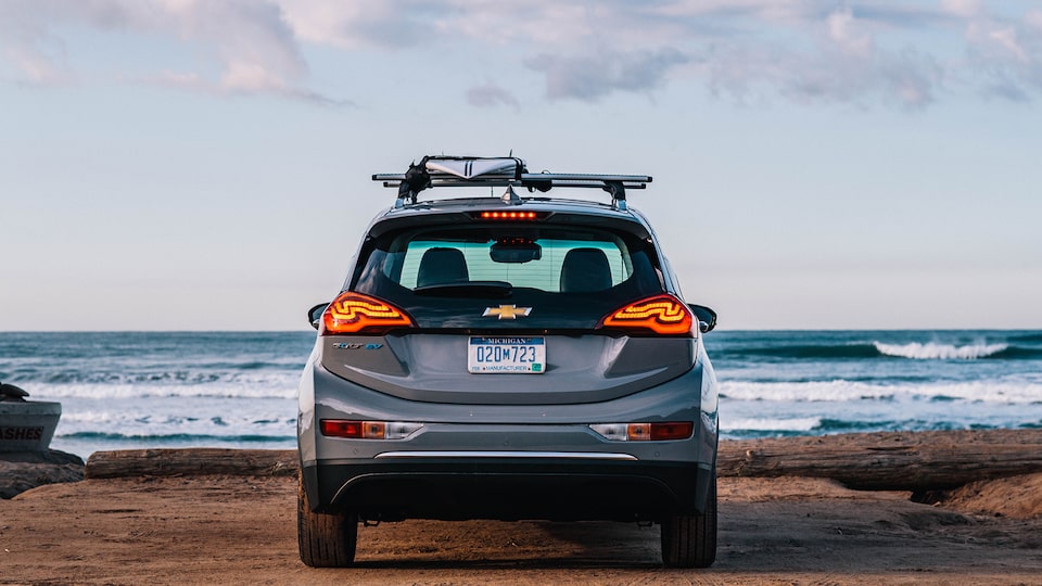 A Bolt EV seen from behind in a beach parking lot looking out at the ocean beyond.