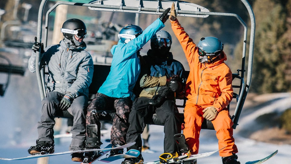 Two people on a chairlift high-five each other while two others look on.